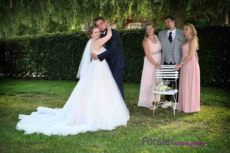 Ein Brautpaar im Hochzeits-Outfit posiert beim Fotoshooting vor der Kamera, drei Trauzeugen stehen daneben