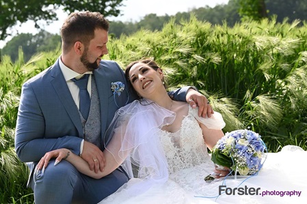 Brautpaar beim Fotoshooting sitzt am Hochzeitstag in einem Kornfeld mit Brautstrauß und schauen sich verliebt an
