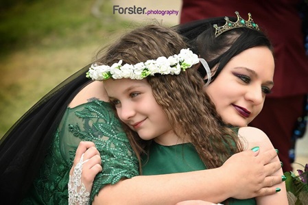 Braut im Hochzeitskleid umarmt beim Fotoshooting ihre Nichte mit Blumenkranz im Haar als Brautjungfer