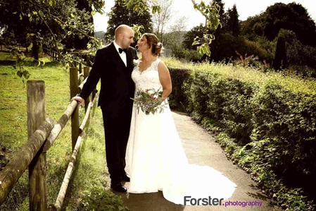 Ein Brautpaar im Hochzeits-Outfit steht beim Fotoshooting an einer Koppel dicht zusammen