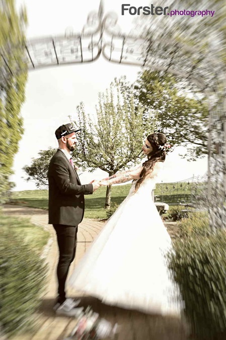 Ein Brautpaar im Hochzeits-Outfit tanzt und posiert beim Fotoshooting in einem Park unter einer Pergola