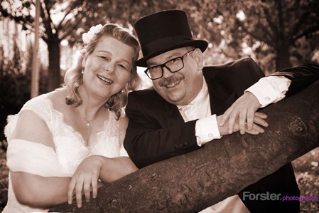 Elegantes Brautpaar lacht beim Hochzeits-Fotoshooting in die Kamera, der Bräutigam trägt einen Zylinder