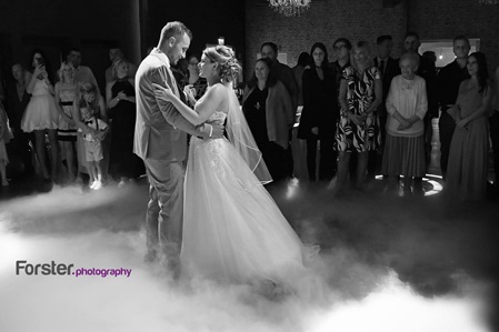 Hochzeitspaar tanzt verliebt miteinander den Eröffnungstanz mit weißem Bodennebel. Gäste im Hintergrund
