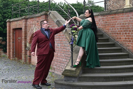 Ein elegantes Hochzeitspaar steht beim Fotoshooting auf einer Treppe an einem Schloss und reichen sich die Hände